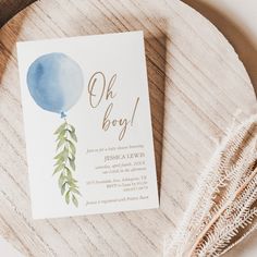 a baby shower is shown on a wooden platter with a blue balloon and greenery