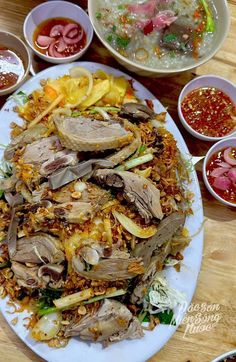 a white plate topped with meat and veggies next to bowls of sauces