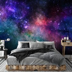 a large bed sitting under a colorful sky filled with stars