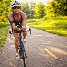 a man riding on the back of a bike down a road next to lush green trees