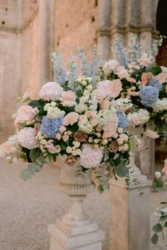 two vases filled with flowers sitting next to each other on top of cement pillars