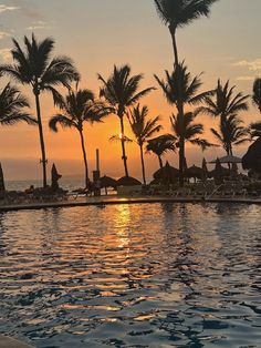 the sun is setting behind palm trees at an outdoor swimming pool with lounge chairs and umbrellas