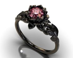 "If you're looking for an engagement ring like no other, stop right here. This AMAZING piece of fine jewelry is the perfect expression of your eternal love. Its BLACK colors bring out the beauty of this ring. This engagement ring is created of gleaming, 14kt black gold, carved into an elaborate leaf design at the top. A striking Pink Sapphire sits boldly at the center, surrounded by black gold petals, forming the eye-catching image of a lotus flower. Item Specifics: (1 Ring Only) Gem Details: Ce Pink And Black Engagement Ring, Black And Pink Wedding Rings, Grunge Engagement Ring, Black Flower Ring For Wedding, Elegant Black Flower Ring For Anniversary, Elegant Black Flower Ring For Wedding, Elegant Black Flower Promise Ring, Elegant Black Flower Ring, Shappire Ring