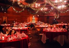 a room filled with lots of tables covered in white and red table cloths next to christmas lights