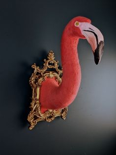 a pink flamingo head mounted to the side of a wall next to a gold framed mirror