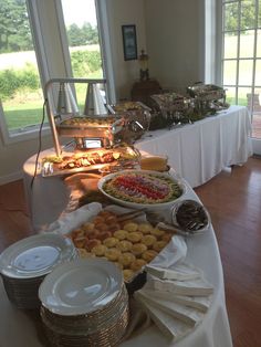 a buffet table filled with lots of food and plates on top of the tables covered in white cloths