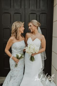 two beautiful women standing next to each other in front of a black door with white flowers