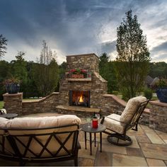 an outdoor fireplace with two chairs and a table in front of it on a patio