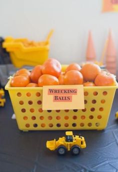 a yellow basket filled with oranges sitting on top of a table next to construction vehicles