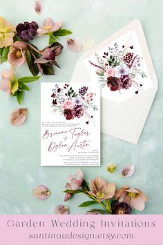 the wedding stationery is surrounded by flowers and greenery on top of an envelope