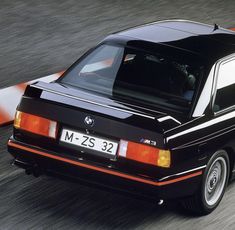 a black car driving down a street next to an orange and white stripe on the road