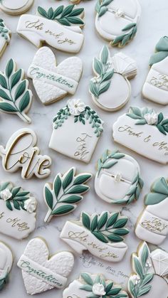 wedding cookies decorated with green leaves and white frosting are displayed on a marble surface