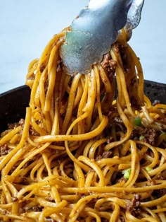 spaghetti being cooked in a skillet with a ladle full of noodles and meat