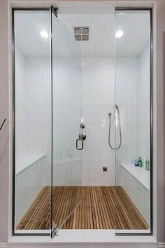 a walk in shower sitting next to a white tiled wall and wooden floored floor