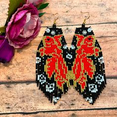 two pairs of beaded earrings on top of a wooden table next to a pink flower