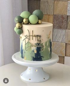 a birthday cake decorated with green and gold balls on a white pedestal in front of a brick wall