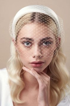 a woman wearing a white veil and holding her hand under her chin, looking at the camera