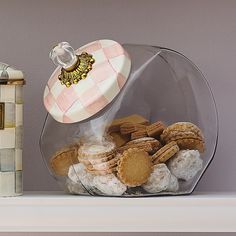 a glass container filled with cookies on top of a white shelf next to a canister