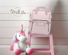 a stuffed unicorn sitting next to a pink bag on a stool with the name stella written on it