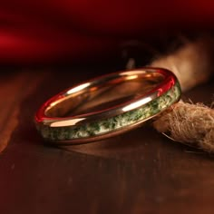 two gold wedding bands with green moss and red enamel inlays on a wooden surface