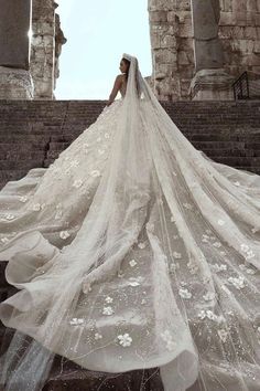 a woman wearing a wedding dress with flowers on the skirt is standing in front of an archway