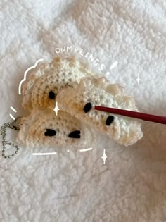 two crocheted teddy bears laying on top of a white blanket next to a red pen