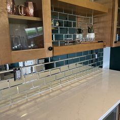 a kitchen counter top with glass tile on the backsplash and shelves above it