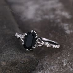 a black diamond ring sitting on top of a gray stone surface with diamonds around it