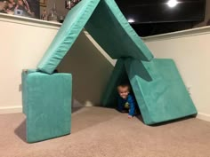 a small child is hiding under a tent in the middle of a room with two couches