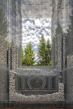 an artistic sculpture made out of rocks and mesh netting with trees in the back ground