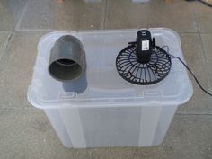 an electric fan sitting on top of a plastic container next to a brown and white dog