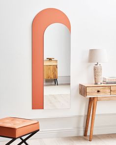 an orange mirror is on the wall next to a small table with a stool and lamp