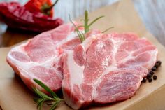 two raw pork chops sitting on top of a piece of brown paper next to peppercorst