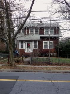 a brown house sitting on the side of a road next to a tree and fence