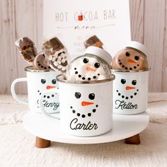 three mugs with snowmen in them sitting on a white plate next to a sign