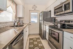 this kitchen has stainless steel appliances and white cabinets, along with an area rug on the floor