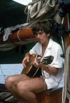 a man sitting on top of a boat holding a guitar