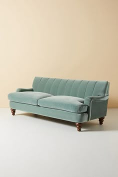 a blue couch sitting on top of a white floor next to a beige wall and wooden legs