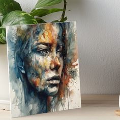 a painting of a woman's face on a table next to a potted plant