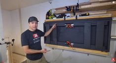 a man standing in front of a black cabinet with tools on it and pointing to the wall