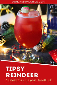 a red drink in a glass on top of a table with pine cones and christmas decorations