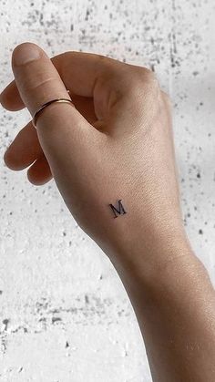 a person's left hand with a small tattoo on the middle finger that reads m