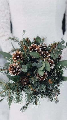 a bride holding a bouquet of pine cones and greenery