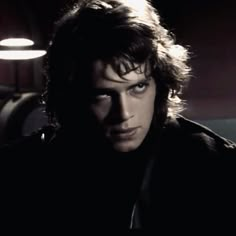 a man with long hair and blue eyes staring at the camera in a dimly lit room