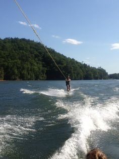 a person on a wake board being pulled by a boat in the water with trees in the background