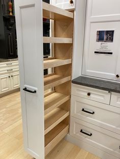 an open pantry door in a kitchen with white cupboards and drawers on both sides