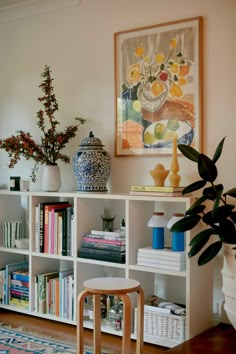 a white bookcase with books and vases on top of it in a living room