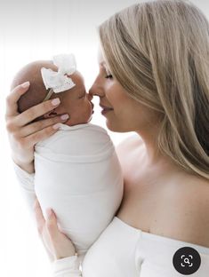 a woman holding a baby in her arms and kissing it's face with the other hand