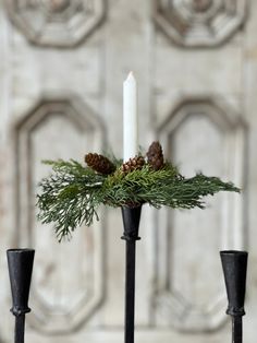 two black candlesticks with pine cones and greenery