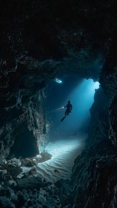 a person in a scuba suit is swimming through a cave with light coming from the ceiling